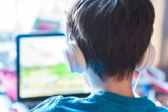 Gaming - Pojke med hörlurar sitter framför bärbar dator och gamear.