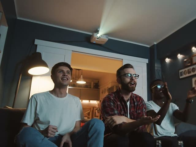 Tre kompisar sitter i en soffa och ser på TV.