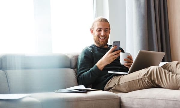 En mand, der bruger sin telefon, mens han har en computer i skødet