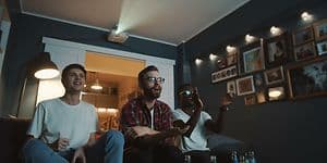 Tre menn som sitter på en sofa i en stue og ser på TV