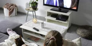 Kvinne som sitter på sofa med katt og ser på TV