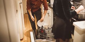 Mann og kvinne på kjøkken. Mannen putter oppvasken i oppvaskmaskinen mens kvinnen lager mat