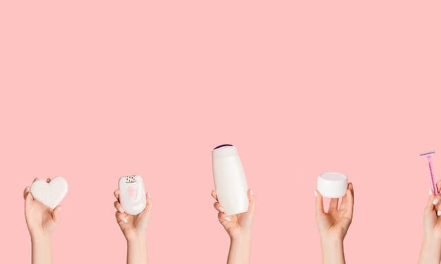 Händer som håller olika hårborttagningsprodukter som epilator, rakapparat, rakhyvel och IPL