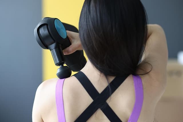  Kvinna som står med ryggen mot oss och använder en massagepistol