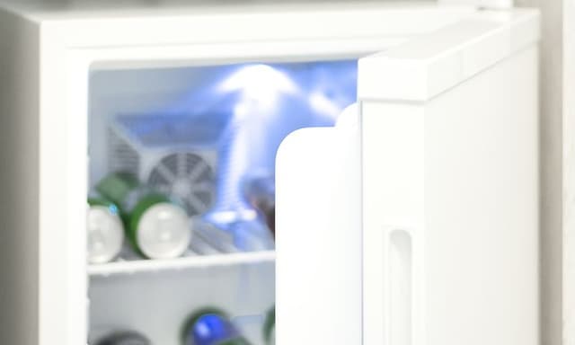 Lähikuva pienestä valkoisesta jääkaapista, jonka ovi on auki ja sisällä erilaisia virvoitusjuomia