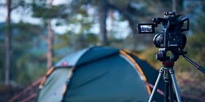Camera on tripods standing in a forest pointing towards a tent