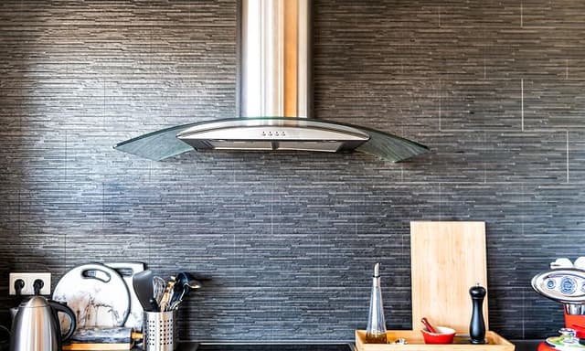 Kitchen fan haning over the stove, with differnt kitchen utitilies beside the stove