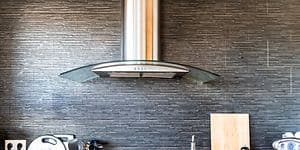 Kitchen fan haning over the stove, with differnt kitchen utitilies beside the stove