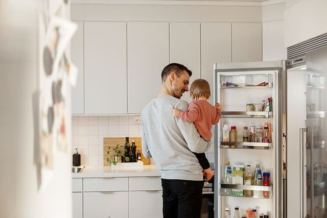 En far og hans datter i deres køkken ved siden af et åbent køleskab
