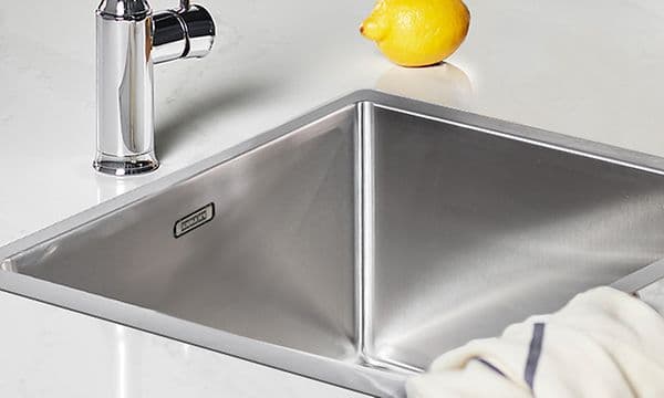 Bild på vit bänkskiva med infälld diskho, med en kökshandduk slängd över kanten och en citron vid sidan. 
