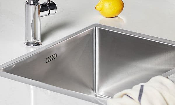Bild på vit bänkskiva med planlimmad diskho, med en kökshandduk slängd över kanten och en citron vid sidan