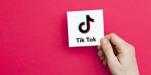 Hånd holder hvitt kort med TikTok-logo på en rosa bakgrunn