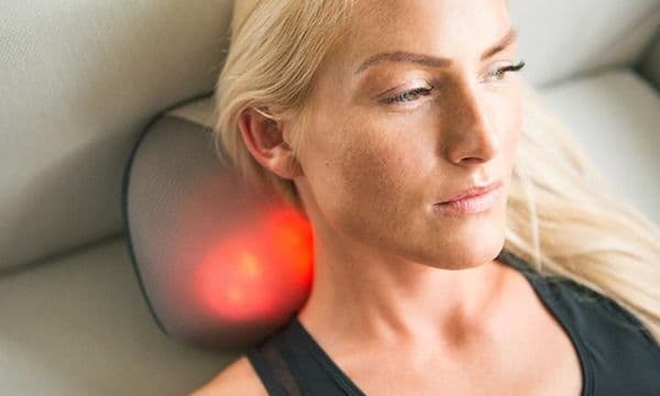 En kvinde, der ligger på sofaen og masserer nakken med YouCare mini-rygmassagepude