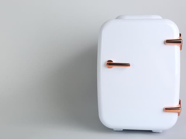  lite, hvitt kjøleskap på lysegrå bakgrunn