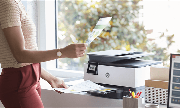 Kvinne holder opp utskrifter ved siden av en HP-printer