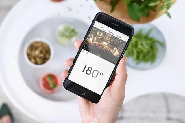 Hånd holder smarttelefon med app som viser smartovn og temperaturen på ovnen på skjermen