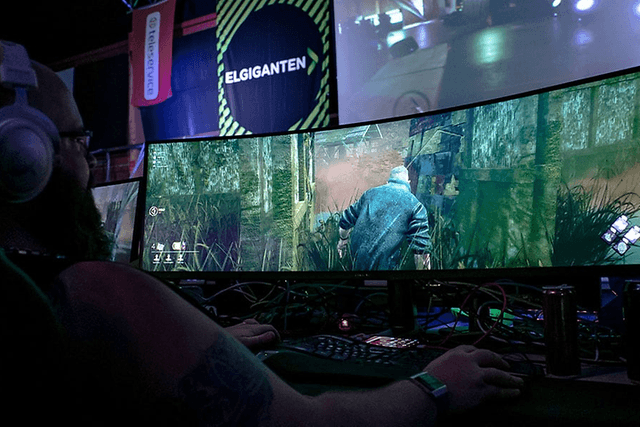 En gamer spiller et spill på en vid gaming-skjerm fra Elkjøp