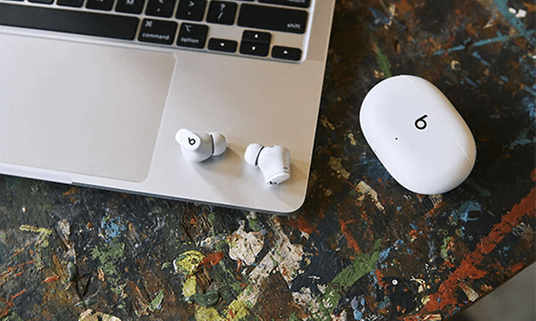 Vita Studio Buds Sound-hörlurar som ligger på en uppfälld Macbook laptop och ett vit fodral ligger bredvid. 