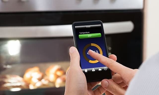 person står foran stekeovn og bruker en app på smarttelefon