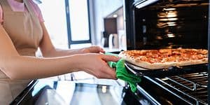 Nainen laittaa pizzaa uuniin