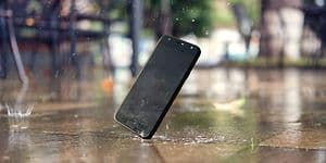 Mobiltelefon som ramlar ner på gatan och träffar asfalten så att skärmen krossas. Regndroppar faller och skvätter vatten. 