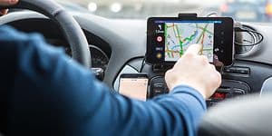 Man som använder en GPS i en bil, pekar med handen på skärmen som sitter vid sidan a ratten. 
