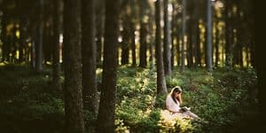kvinne kledd i hvite klær leser en bok i skogen
