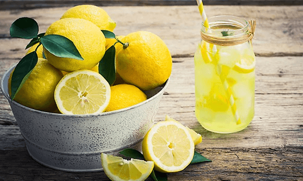 Ett glas med lemonade bredvid en skål med citroner på ett bord. 