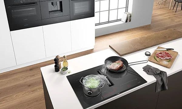 Bild ovanifrån på köksö med induktionshäll med inbyggd frånluftsfläkt och matlagning på gång på spisen. 