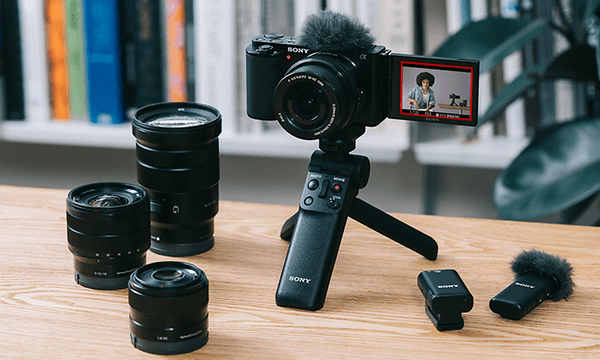 Kamera på en liten tripod med olika objektiv och tillbehör bredvid den
