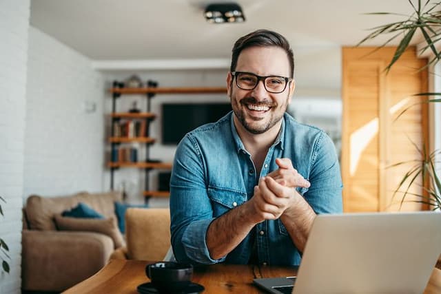 Smilende mand sidder ved sin bærbar computer