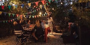 Kvinna tar en bild av flera personer som samlats på en trädgårdsfest bland träden med ljusslingor och vimplar. 