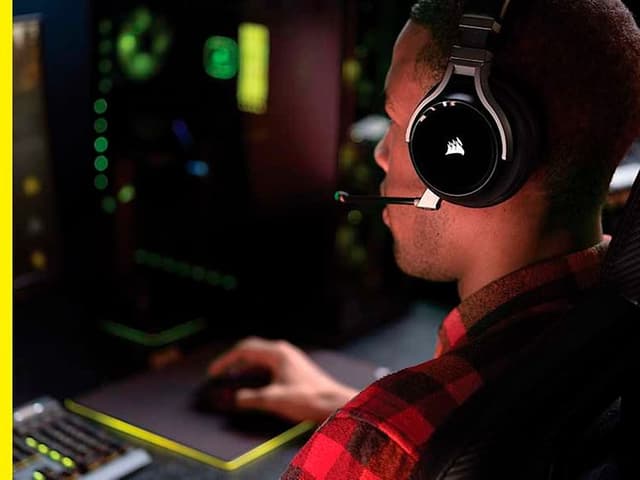 Man som sitter framför dator och spelar och har på sig ett svart gaming-headset från Corsair.