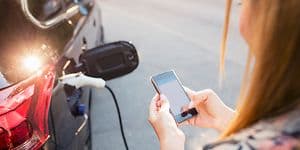 Kvinde holder en smartphone, imens hun oplader bilen