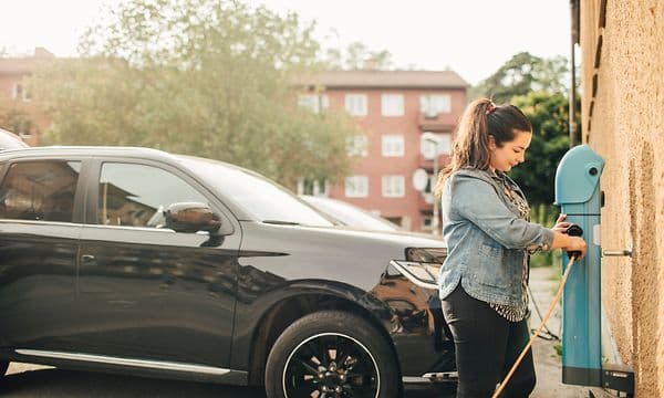 Kvinna håller i laddningskabel från laddstation vid en parkering