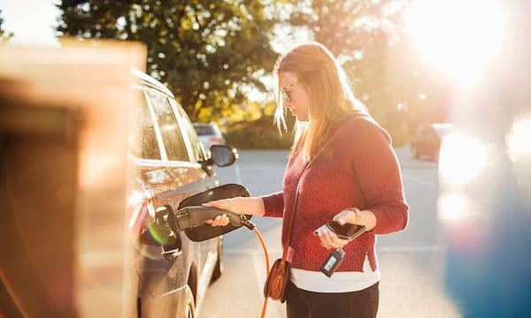  Kvinna som laddar en svart elbil på en parkeringsplats