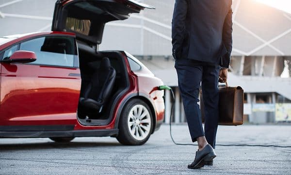Man med portefølje som går mot en åpen rød Tesla