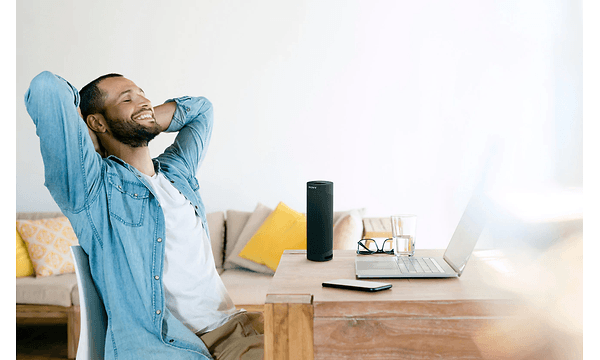 smilende mann lener seg bakover ved bord med laptop og smarttelefon