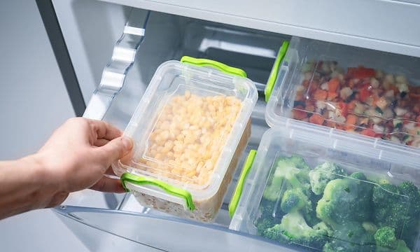 Käsi ottamassa laatikollista maissia järjestetystä pakastimesta