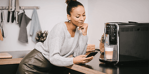 En kvinde med en smartphone foran sin Melitta kaffemaskine