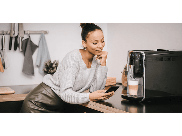 En kvinne med en smarttelefon ved siden av en Melitta kaffemaskin