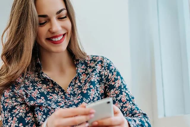 Smilende kvinde, der sidder med sin telefon I hånden