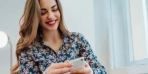 Smilende kvinde, der sidder med sin telefon I hånden