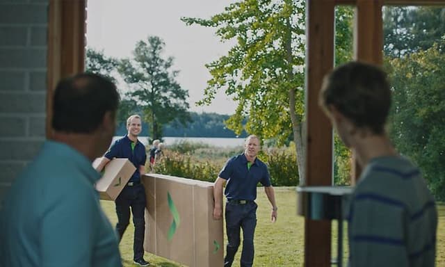 Mies ja poika katselevat ikkunasta Gigantin työpukuun pukeutuneita miehiä, jotka kantavat uutta televisiota sisälle