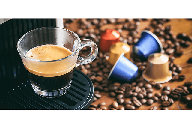 En kop espresso fra en kapselkaffemaskine med kapsler og kaffebønner på disken
