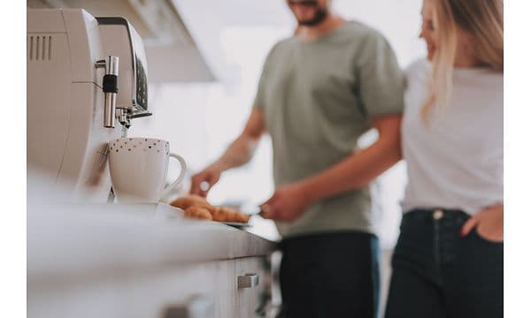 En kaffemaskine og et par, der står i baggrunden