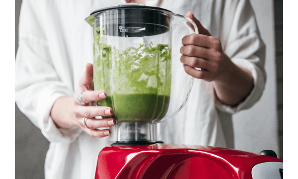 Person laver en grøn smoothie i en rød blender