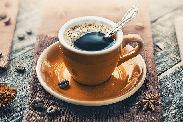 En kopp espresso med fat och kaffebönor runt omkring.