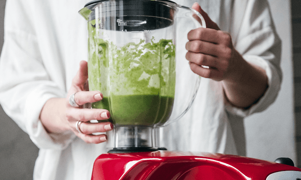 person lager en grønn smoothie i en rød blender