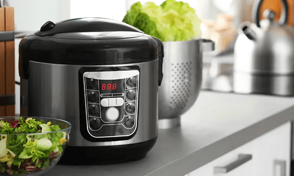en svart slow cooker på en kjøkkenbenk med en grønn salat foran på benken